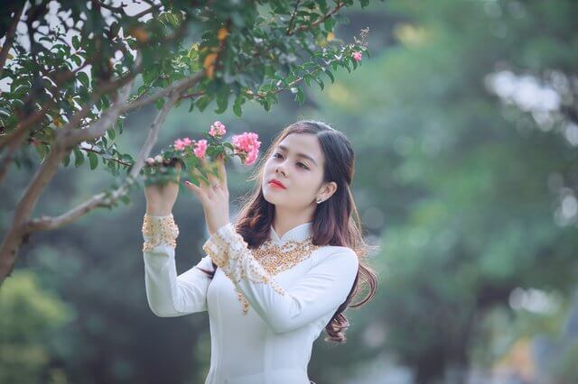 Pretty oriental young girl wearing white dress in flower garden